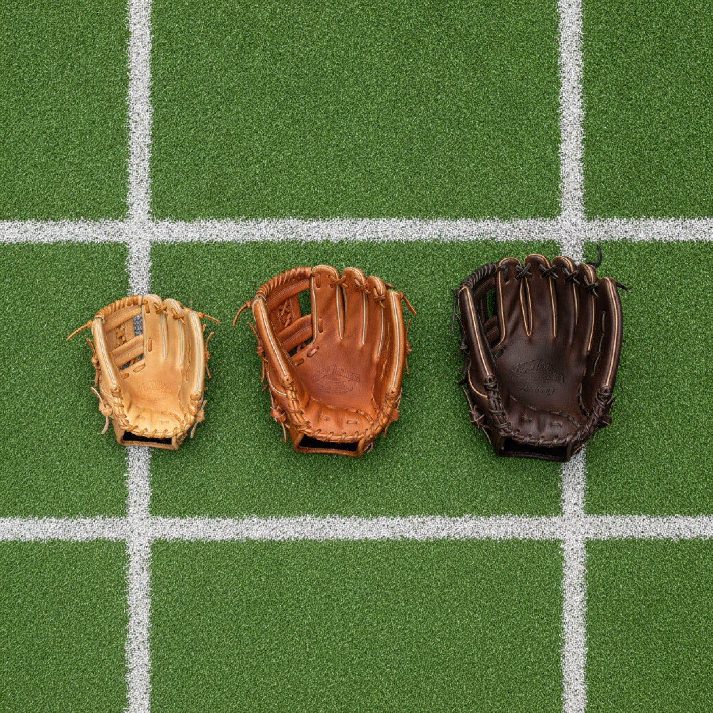 Three leather baseball fielding gloves arranged from smallest youth size to largest adult size on green baseball turf, showing how glove size grows with a player.