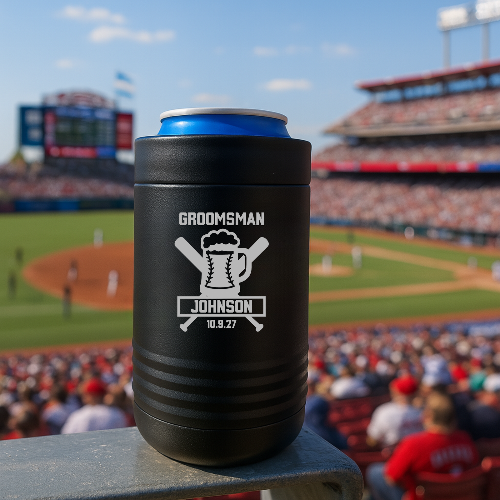 Black stainless steel can cooler with laser-engraved "GROOMSMAN," beer mug and baseball bat design, sample name "JOHNSON," and date "10.9.27," displayed at baseball stadium.