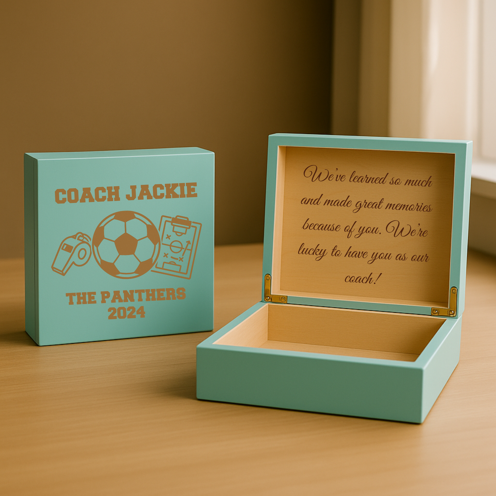 Turquoise wooden keepsake box with sample engraving "Coach Jackie" and soccer graphics on lid; interior shows personalized message example and empty storage compartment with brass