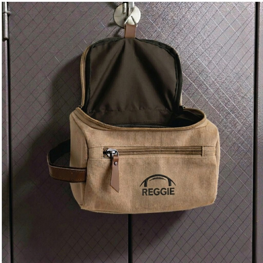 Personalized football toiletry bag in washed canvas with a leather handle and an embroidered football with custom initials, built for road games and college