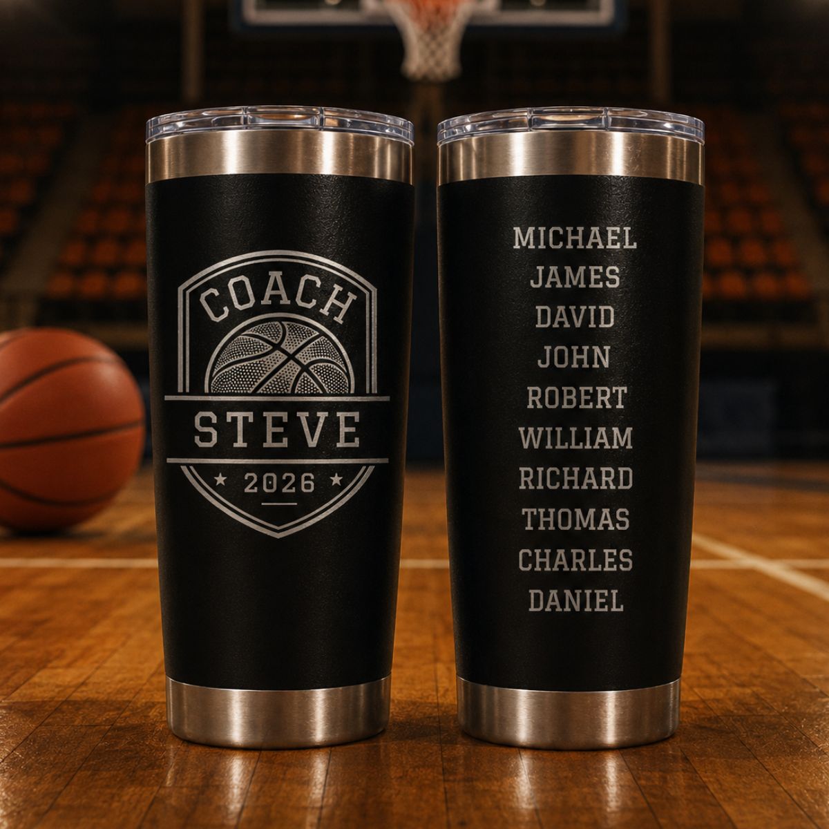 Two black basketball coach tumblers on a hardwood court, one engraved with a basketball shield reading Coach Steve 2026 and the other with ten player names down the back