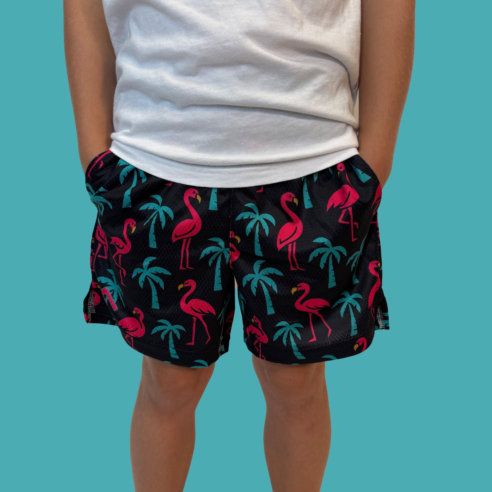 Person wearing white t-shirt and black shorts with neon pink flamingos and teal palm tree print on turquoise background