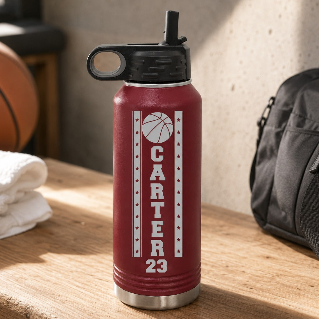 Maroon personalized basketball player water bottle engraved with a basketball, the name Carter down the center and the jersey number 23, on a locker room bench