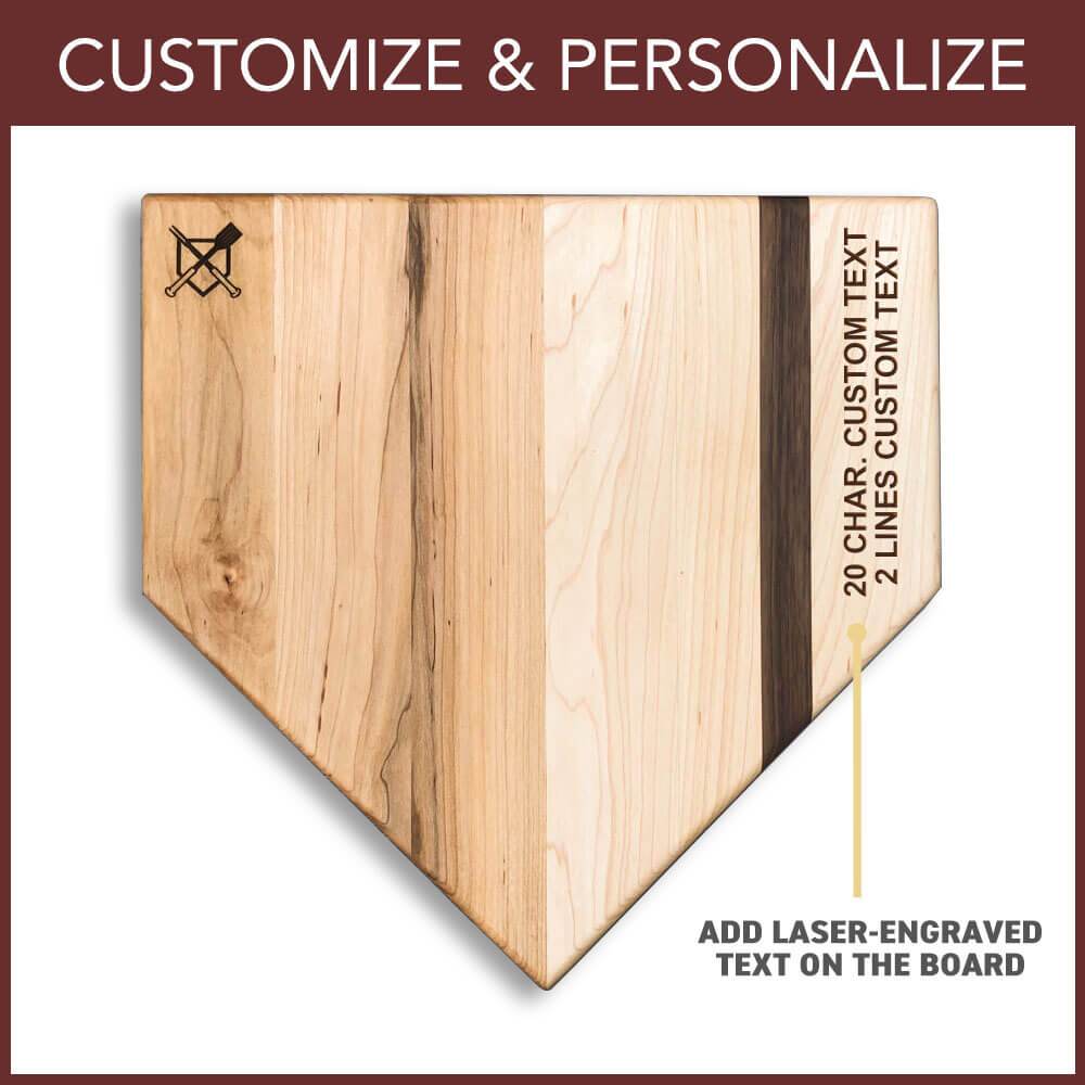 Natural wood home plate cutting board with sample laser-engraved text showing customization area on right edge, featuring crossed baseball bats icon on upper left corner