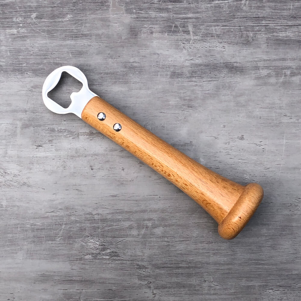 The PICKOFF bottle opener laid flat on a gray concrete surface, showing the full bat-knob handle and steel opener head