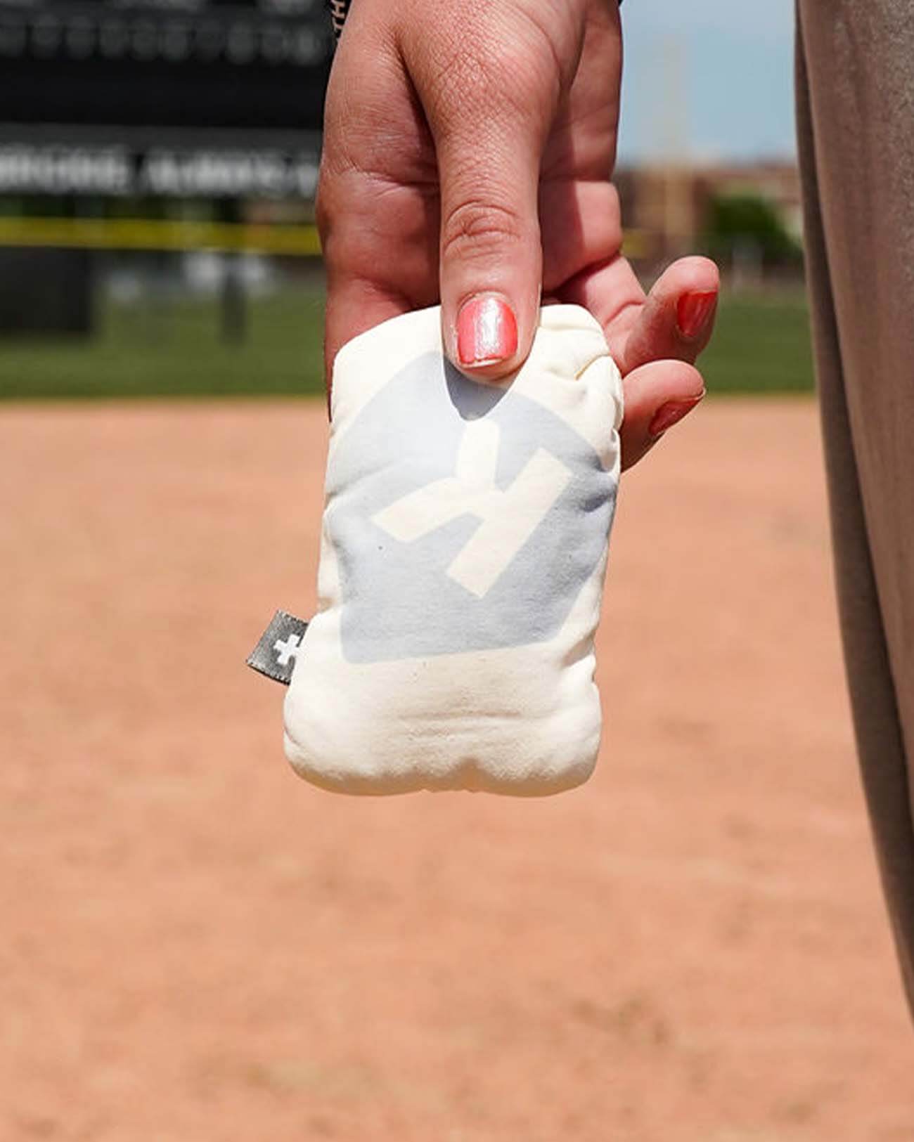 Hand holding white rosin bag with sample number printed on front, displayed on baseball field infield dirt background