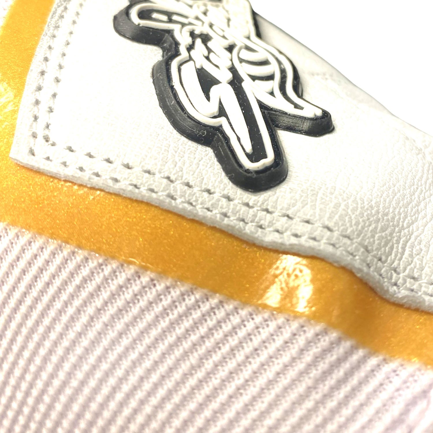 Close-up of white sheepskin leather batting glove with black and white team logo patch and gold trim detail along the wrist cuff.