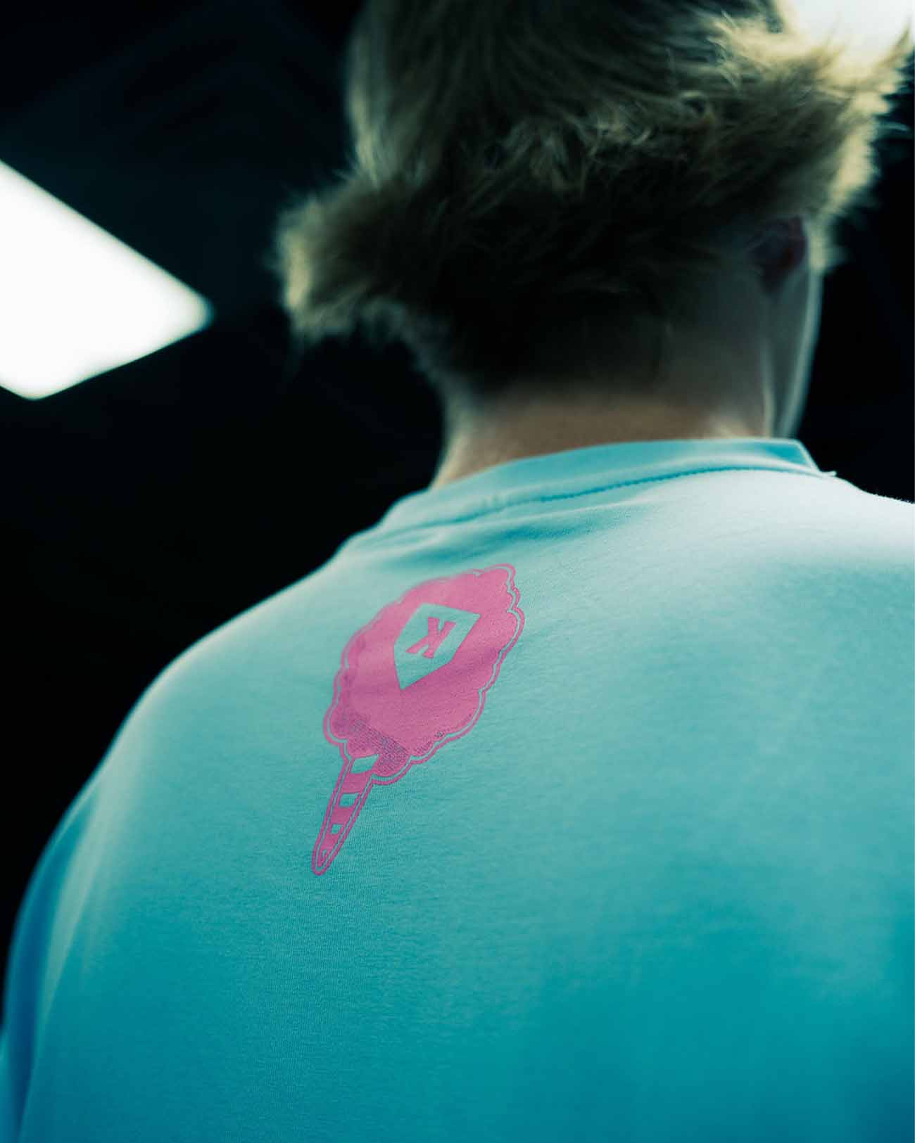 Person wearing turquoise cotton tee with pink embroidered baseball glove and pitcher logo on back shoulder area