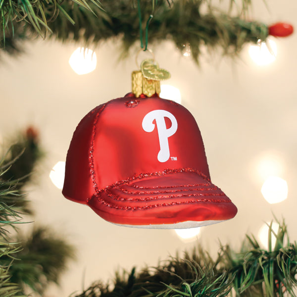 Red baseball cap ornament with white Phillies "P" logo, hanging from evergreen garland with white lights