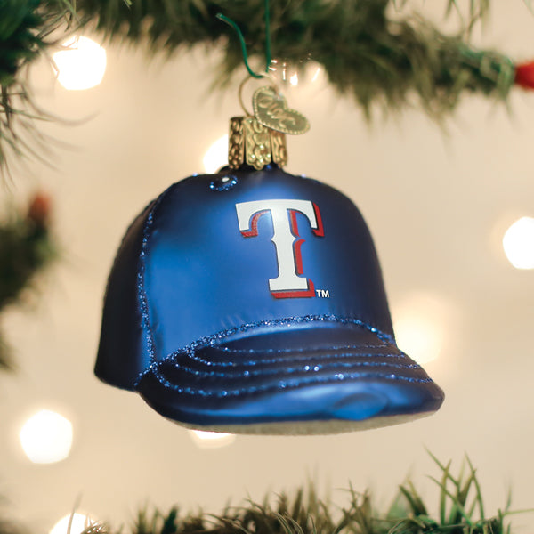 Blue baseball cap ornament with red and white "T" logo hanging from evergreen branch with bokeh lights in background