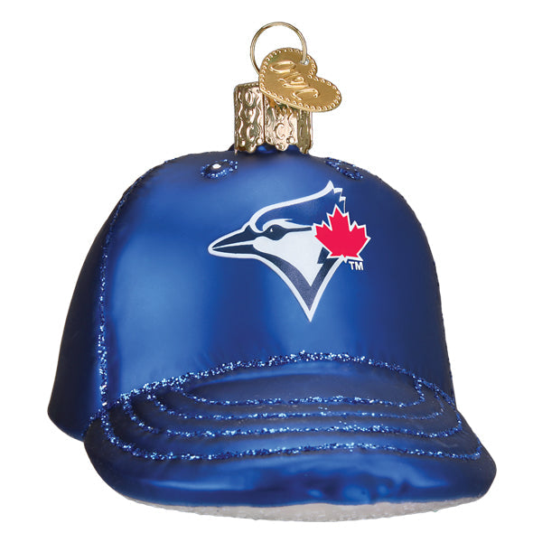 Blue glass ornament shaped like a baseball cap with Toronto Blue Jays logo, white bird outline and red maple leaf, featuring glitter detail on visor and golden cap topper