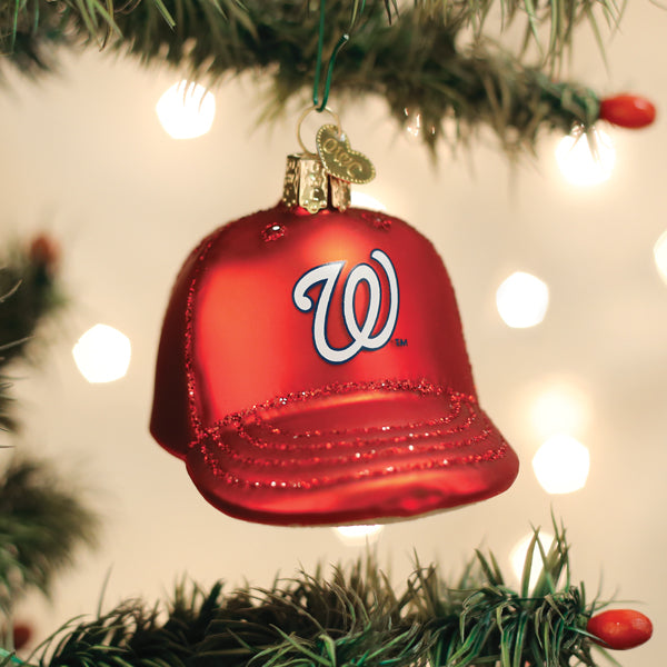 Red baseball cap ornament with embroidered "W" logo hanging from evergreen garland with bokeh lights in background