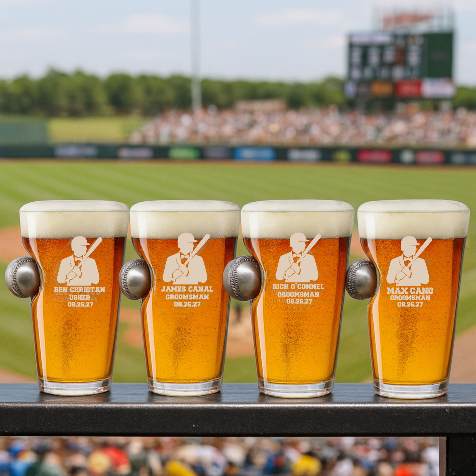 Four personalized pint glasses with engraved sample names "Ben Christian Usher," "James Canal Groomsman," "Rich O'Connell Groomsman," and "Max Cano Groomsman" with date 08.26.27, each featuring an embedded baseball, displayed at a baseball stadium.