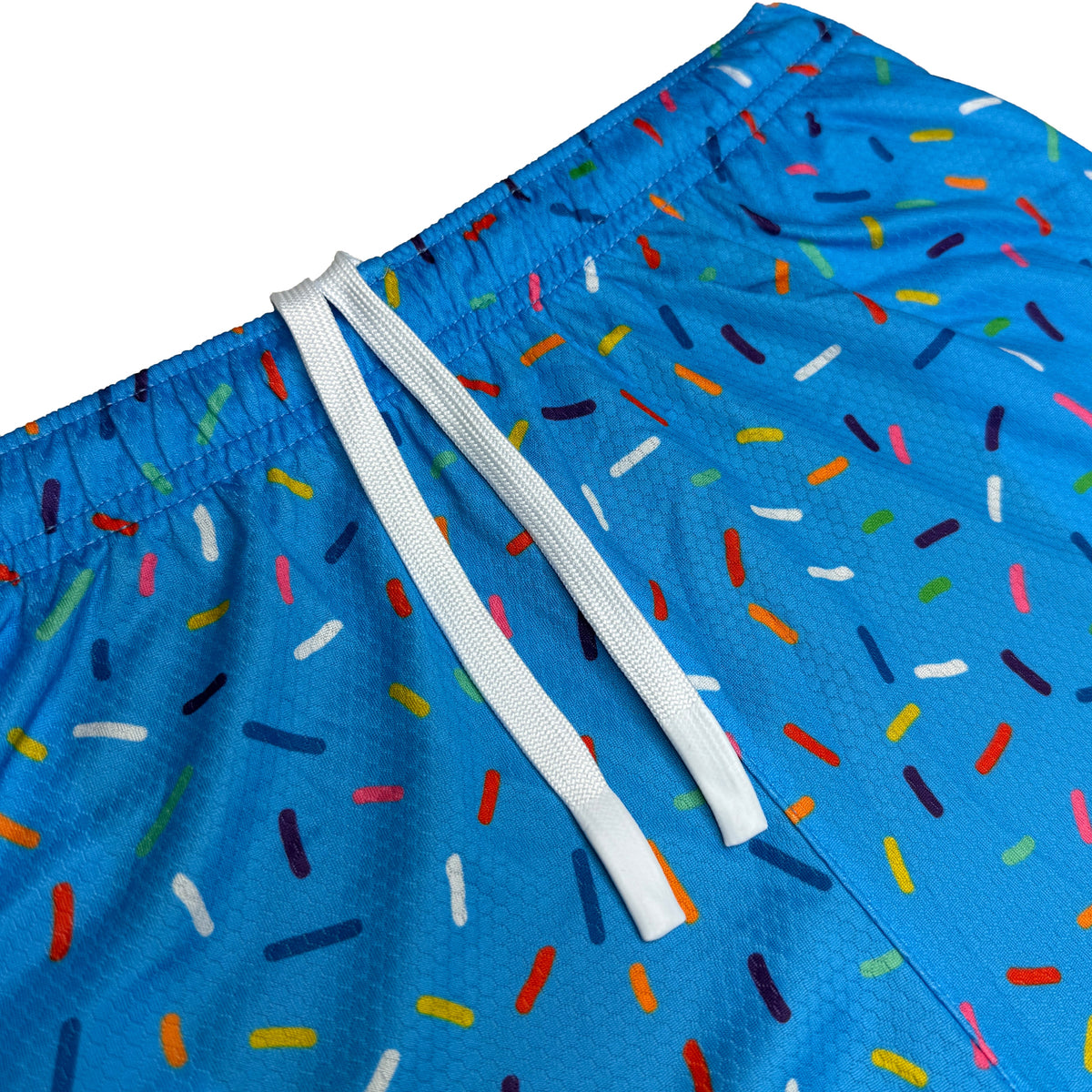 Blue athletic shorts with colorful sprinkle pattern, white drawstring, and elastic waistband visible from angled side view