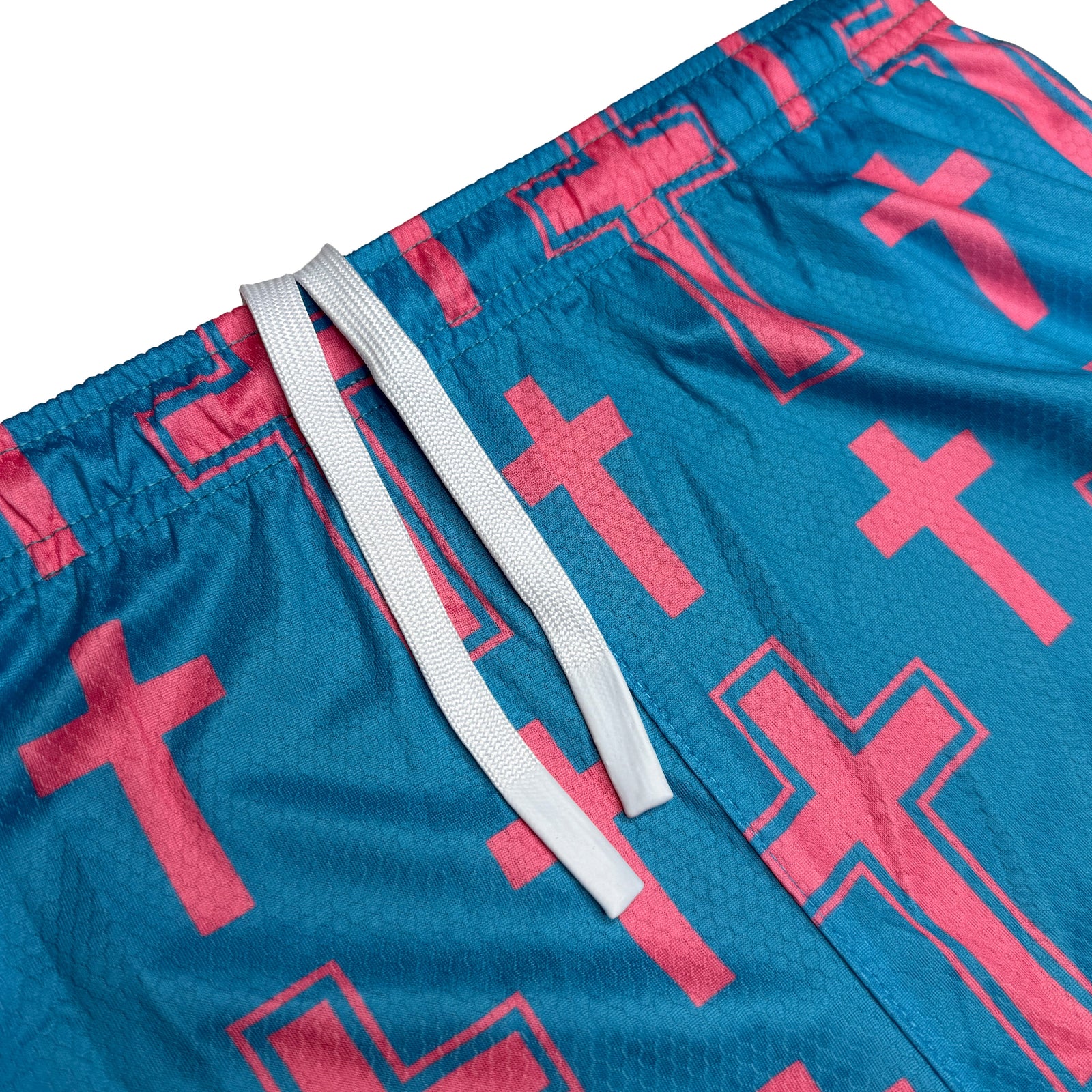 Teal athletic shorts with pink cross pattern and white drawstring detail showing waistband and side seam construction.