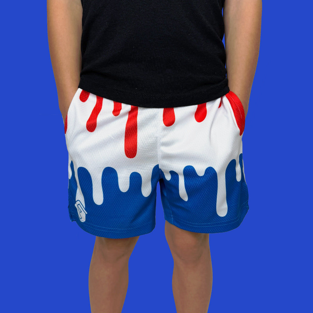 Person wearing red, white, and blue drip-design athletic shorts with deep side pockets and elastic waistband against blue background