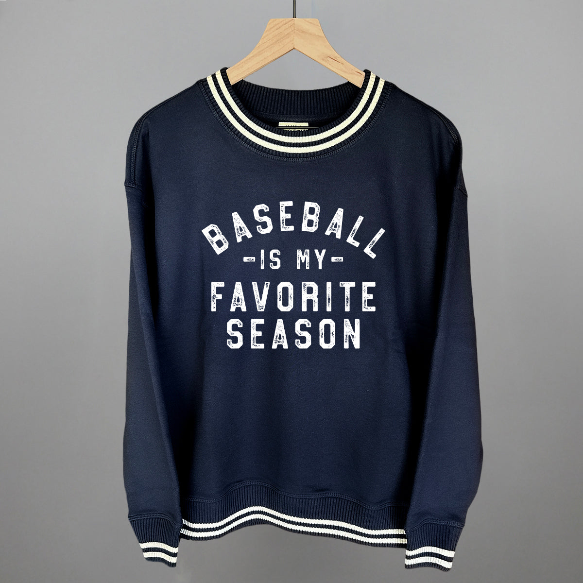 Navy crewneck sweatshirt with white striped ribbed trim at neckline, cuffs, and hem, printed with "Baseball Is My Favorite Season" text in white
