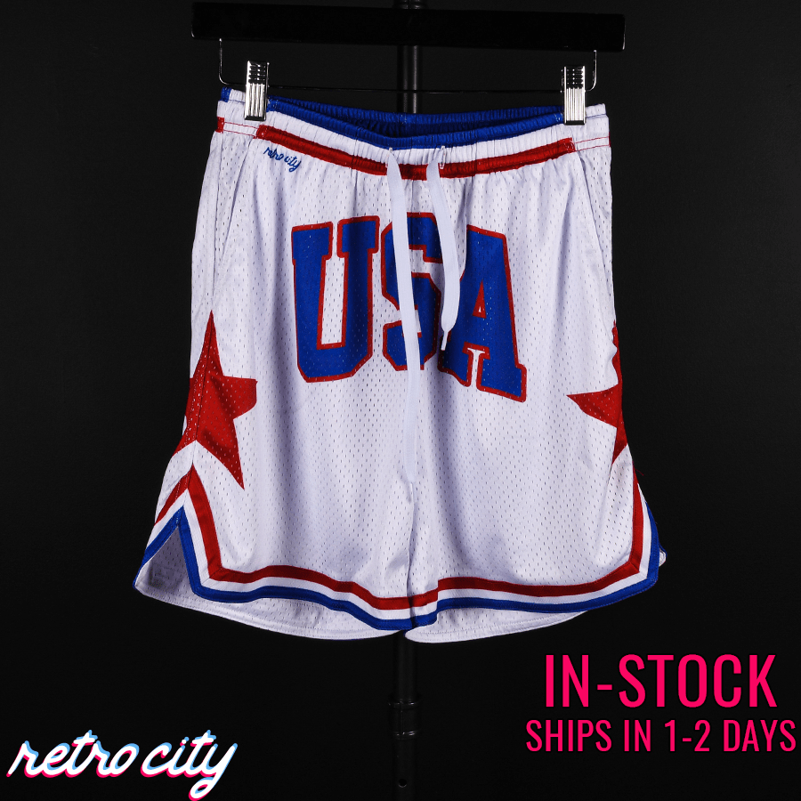 White mesh shorts with blue and red "USA" graphic on front, red stars on sides, and blue and red striped trim at waistband and leg openings.
