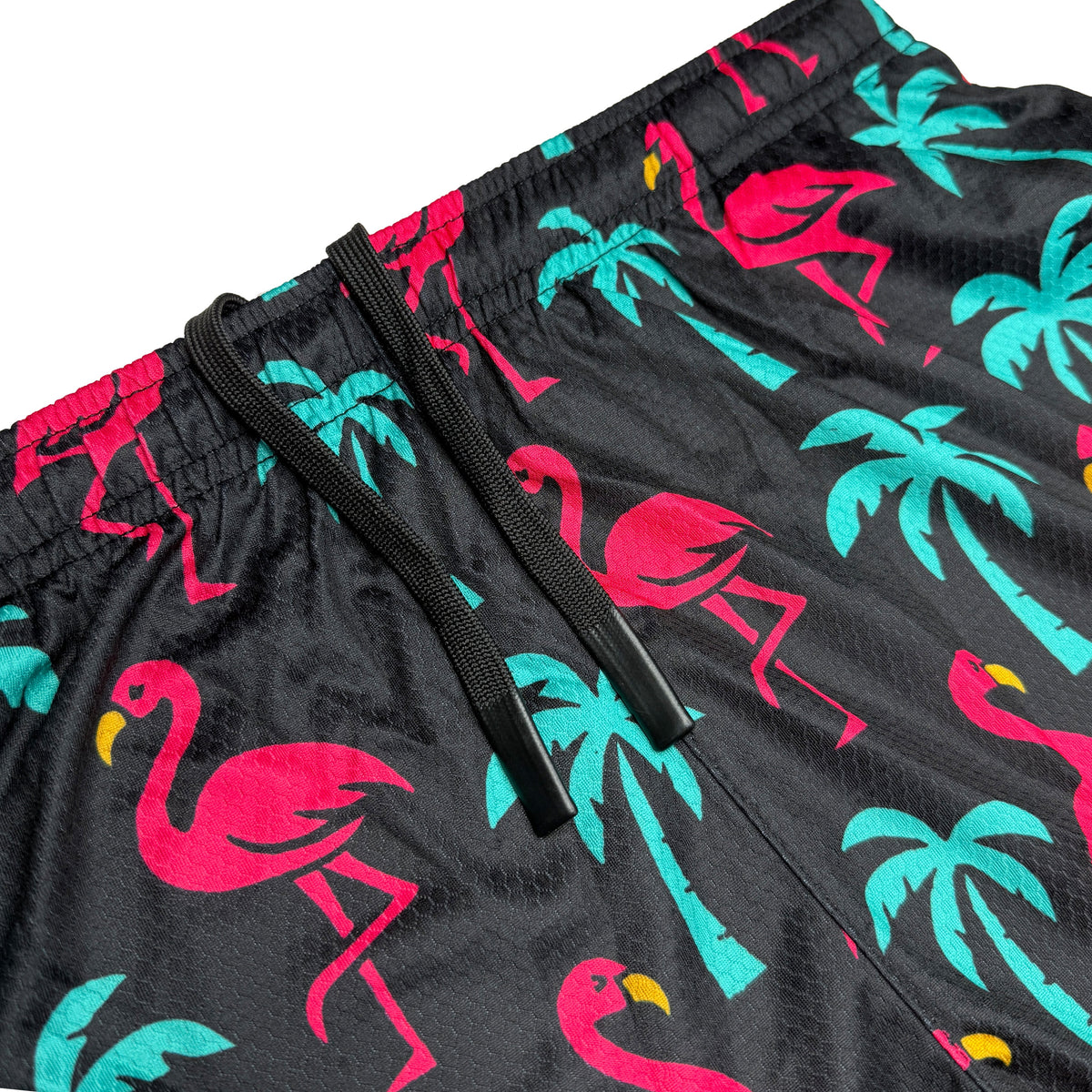Black shorts with pink flamingo and turquoise palm tree print, showing elastic waistband with black drawstring and side pocket detail.