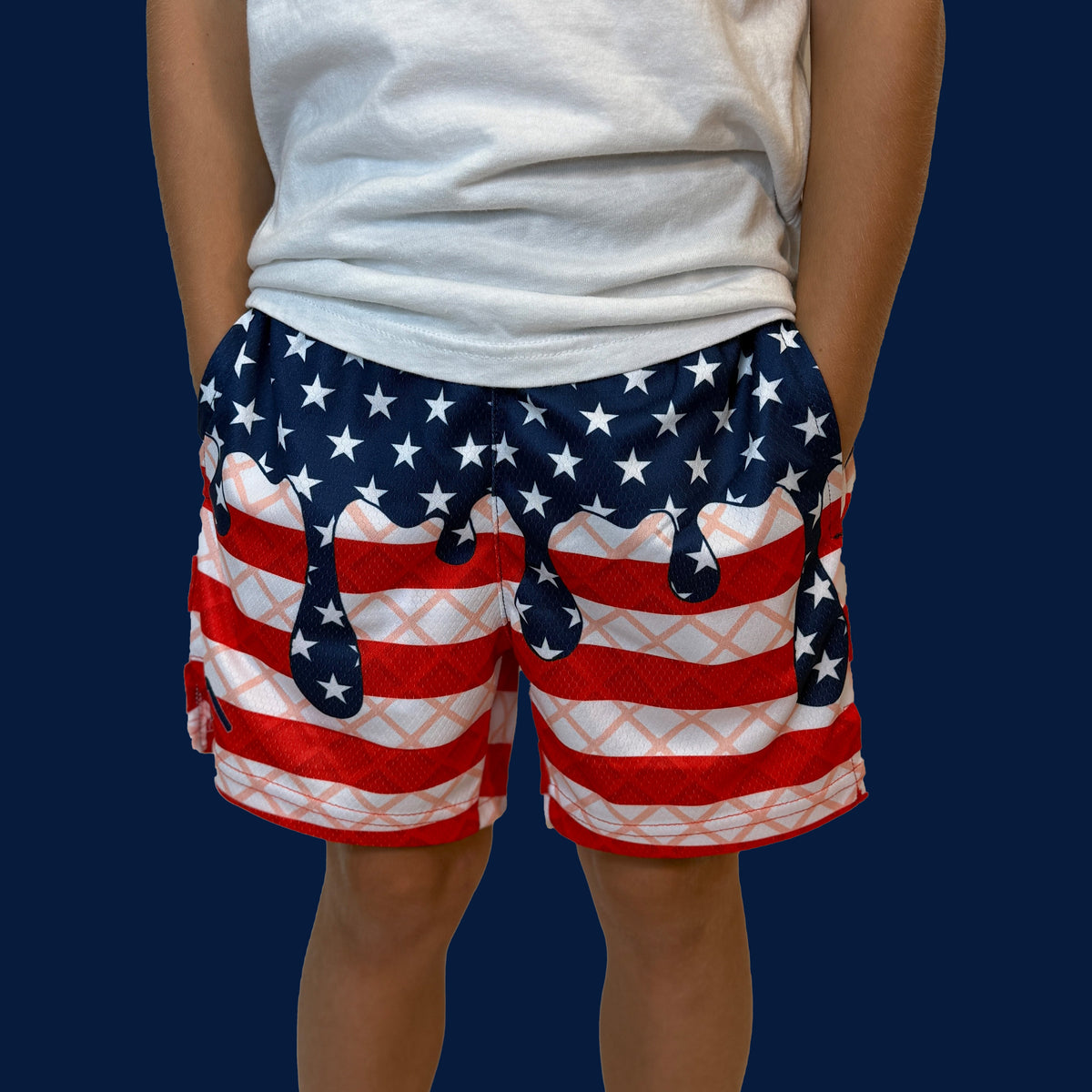 Person wearing USA flag-patterned shorts with red and white stripes, white stars on navy blue upper section, paired with white t-shirt against blue background