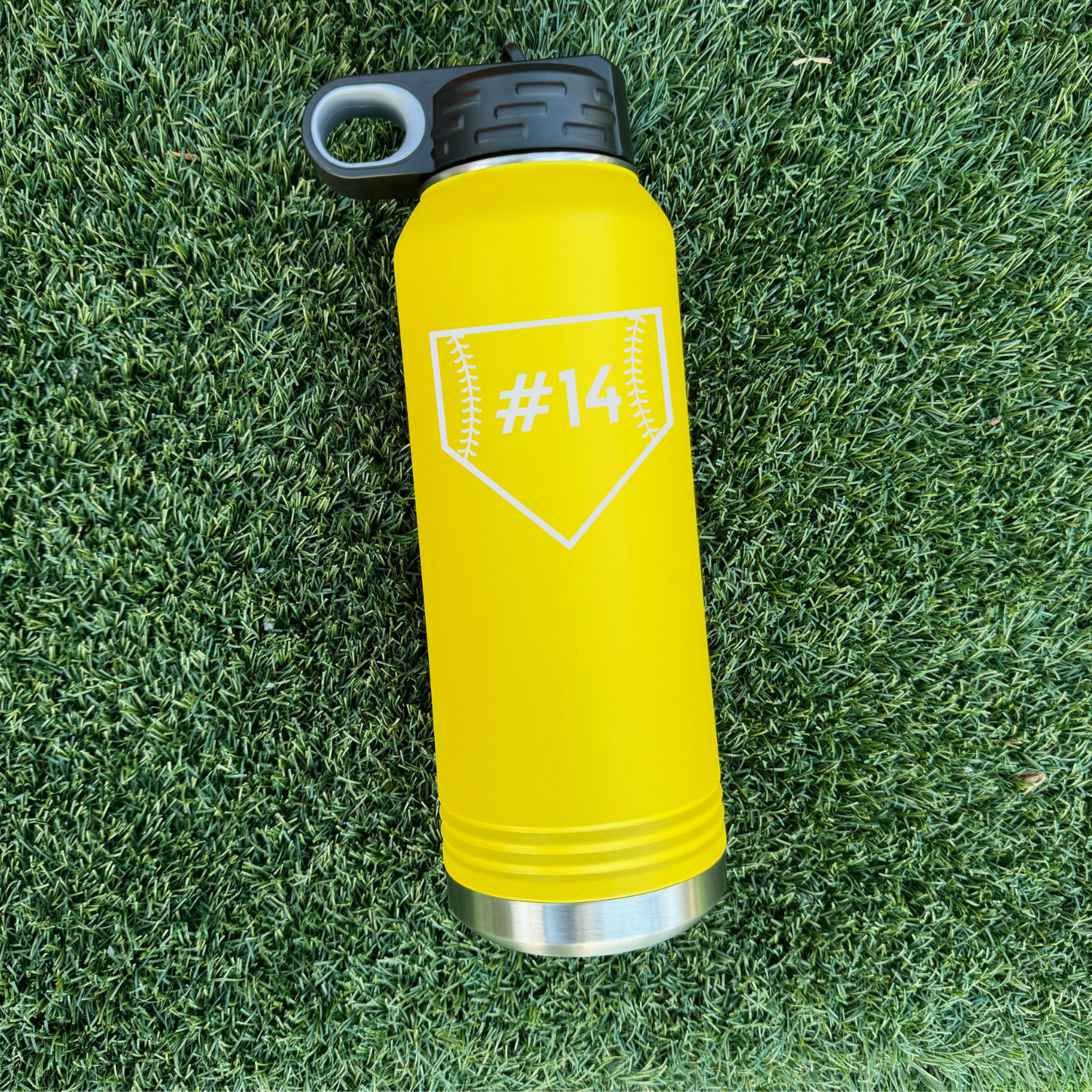 Bright yellow water bottle with stainless steel base and black screw lid, engraved with sample number #14 in home plate design on front, positioned on grass field background.