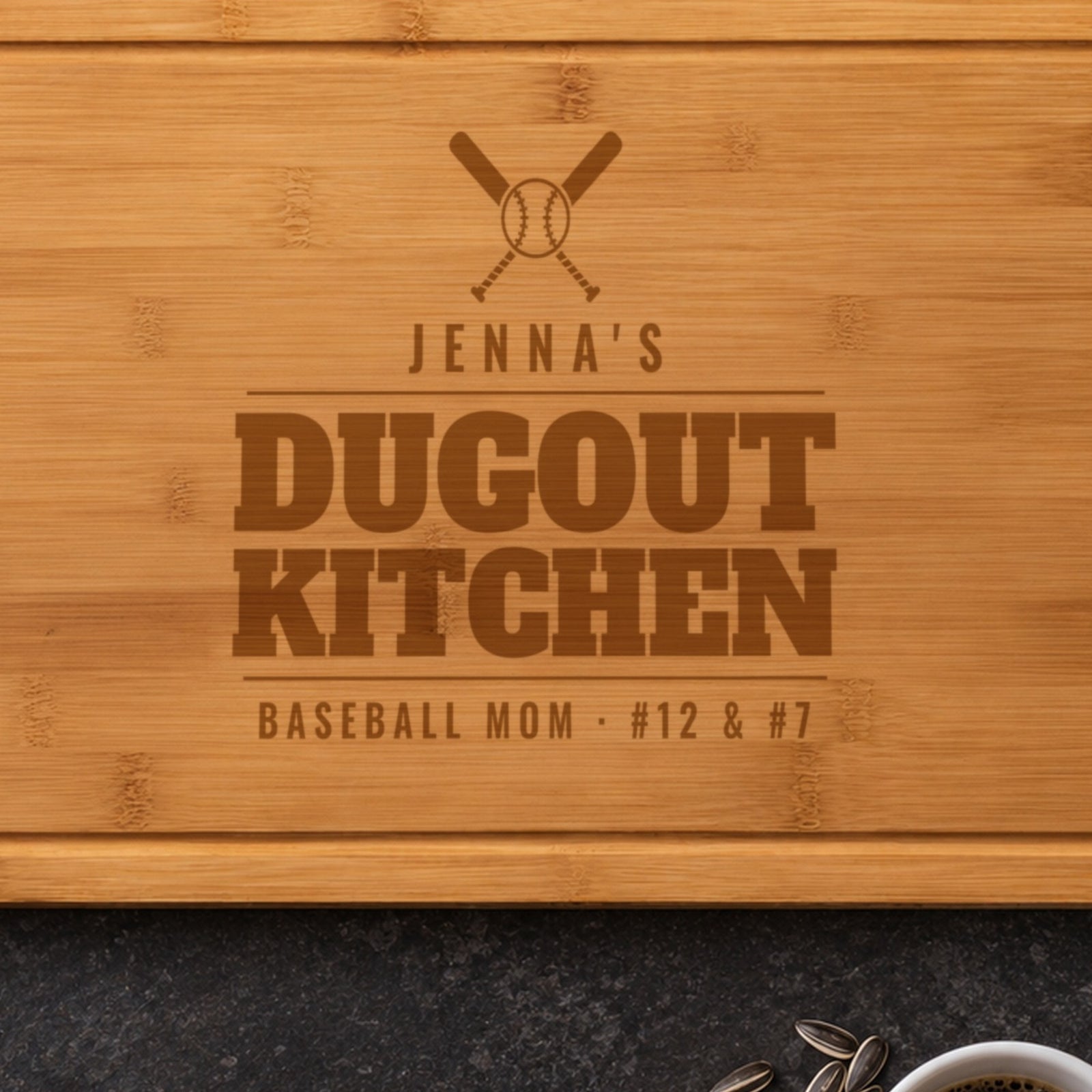 Close-up of the laser engraved baseball mom cutting board: crossed bats, a baseball, JENNA'S and DUGOUT KITCHEN burned into the bamboo