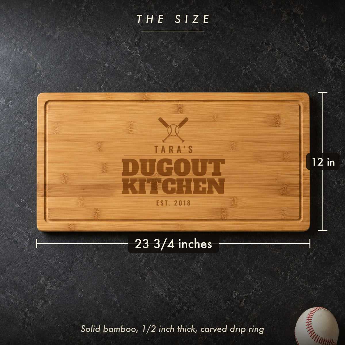 Size of the baseball mom cutting board, 23 3/4 inches long by 12 inches wide in half inch solid bamboo, on a dark kitchen counter with a baseball
