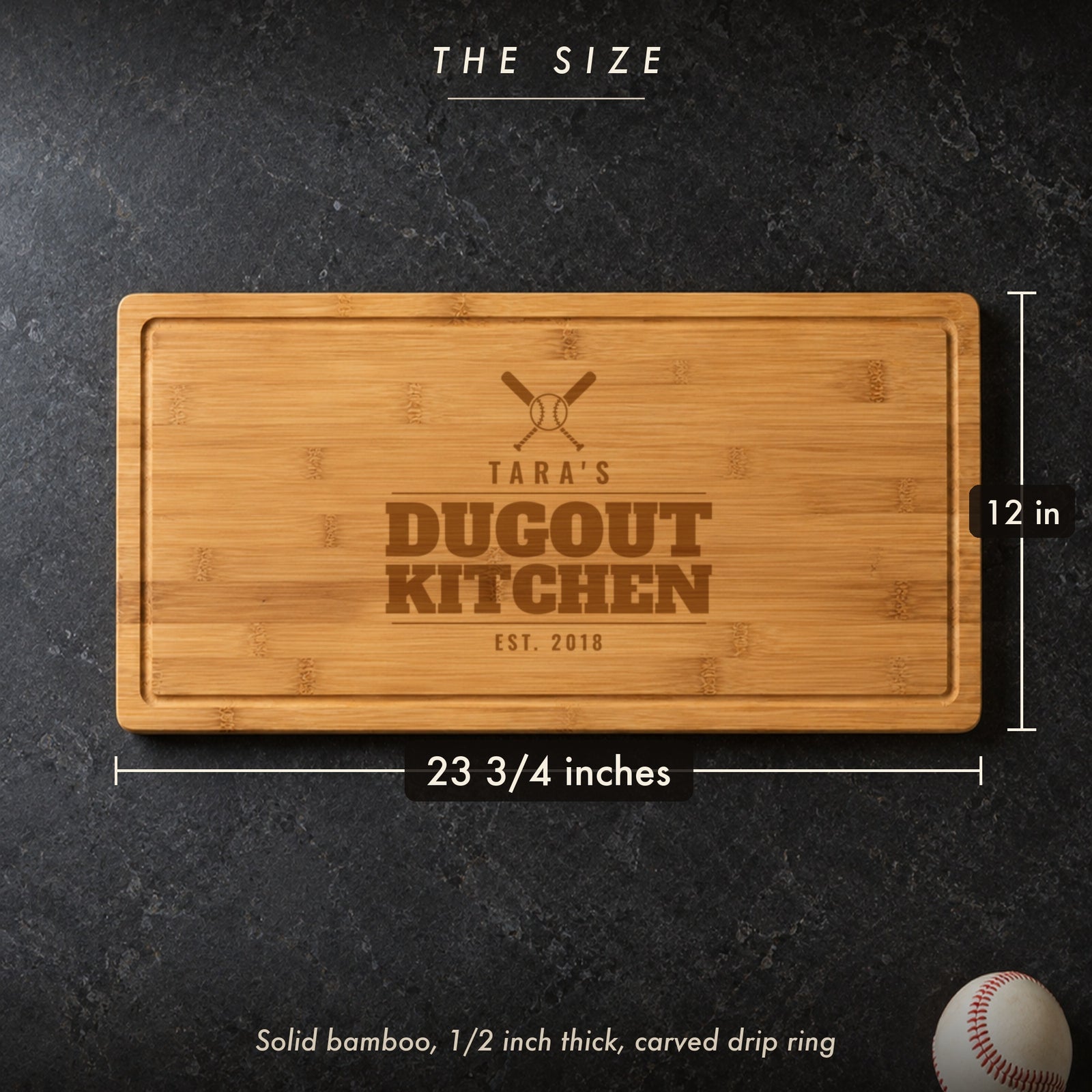 Size of the baseball mom cutting board, 23 3/4 inches long by 12 inches wide in half inch solid bamboo, on a dark kitchen counter with a baseball