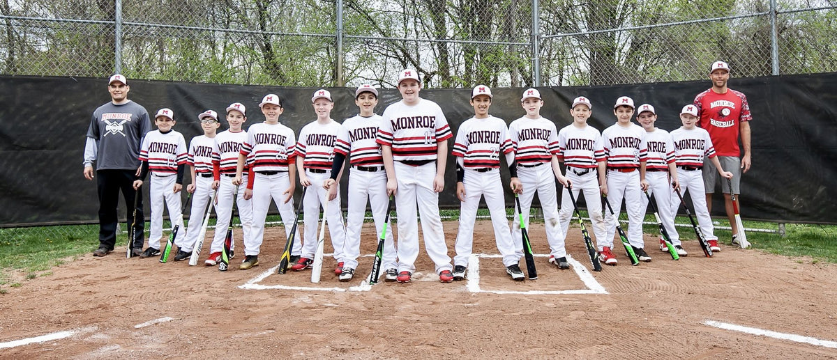 The Monroe youth baseball team lined up at home plate with their bats, with Chris Bajda of Batter Box Sports standing on the right in a red Monroe Baseball shirt