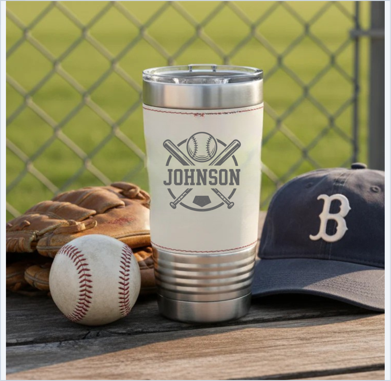 Cream and stainless steel tumbler engraved with sample name "JOHNSON" and baseball crossed bats design, displayed with baseball glove, ball, and cap.