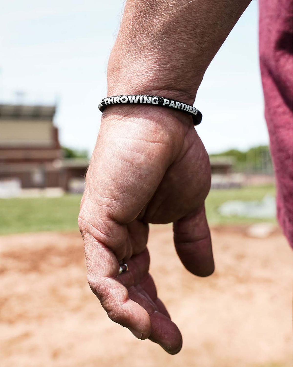 Adult nylon bracelet with screen-printed text reading "Throwing Partners" worn on wrist at a baseball field