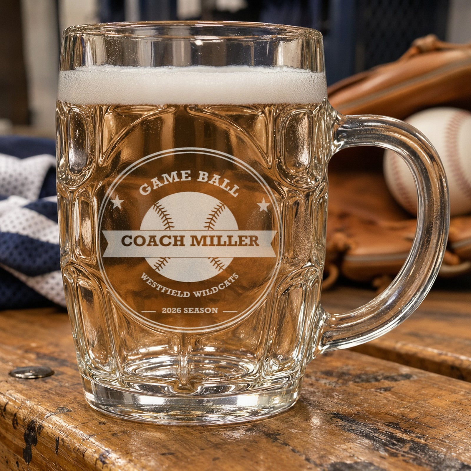 Engraved baseball coach beer stein full of lager on a worn dugout bench next to a leather glove, etched Game Ball, Coach Miller, Westfield Wildcats, 2026 Season