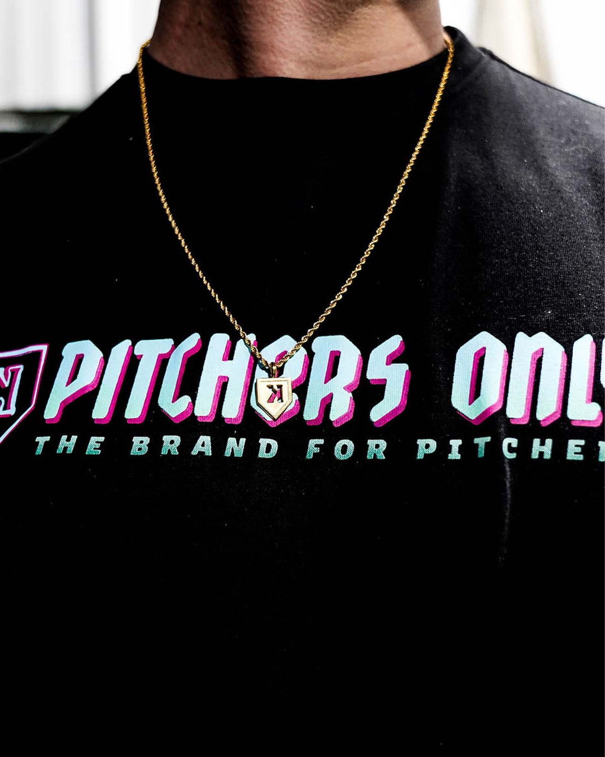 Gold-plated K pendant necklace worn on black t-shirt, showing backwards K design and rope chain detail in lifestyle context.