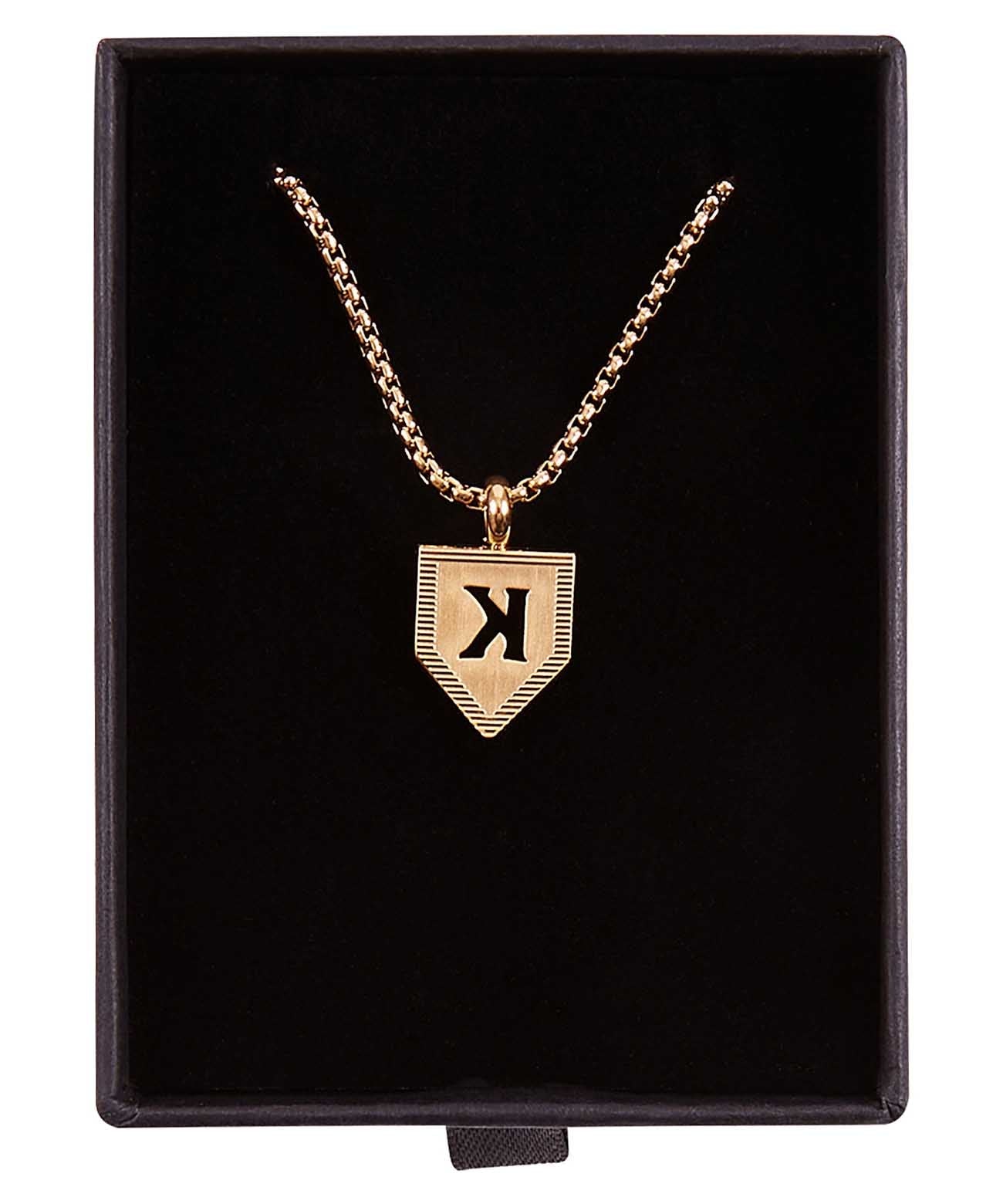 Gold-plated pendant necklace with sample letter K engraved on shield-shaped charm, displayed in black velvet box with rope chain.