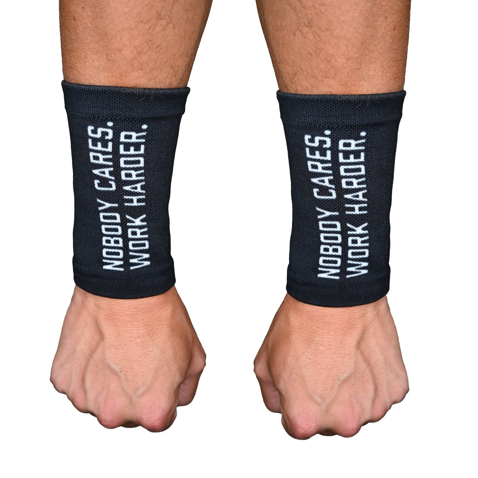 Pair of black wrist support sleeves worn on a man's wrists, printed with white text reading "NOBODY CARES. WORK HARDER." on each sleeve.