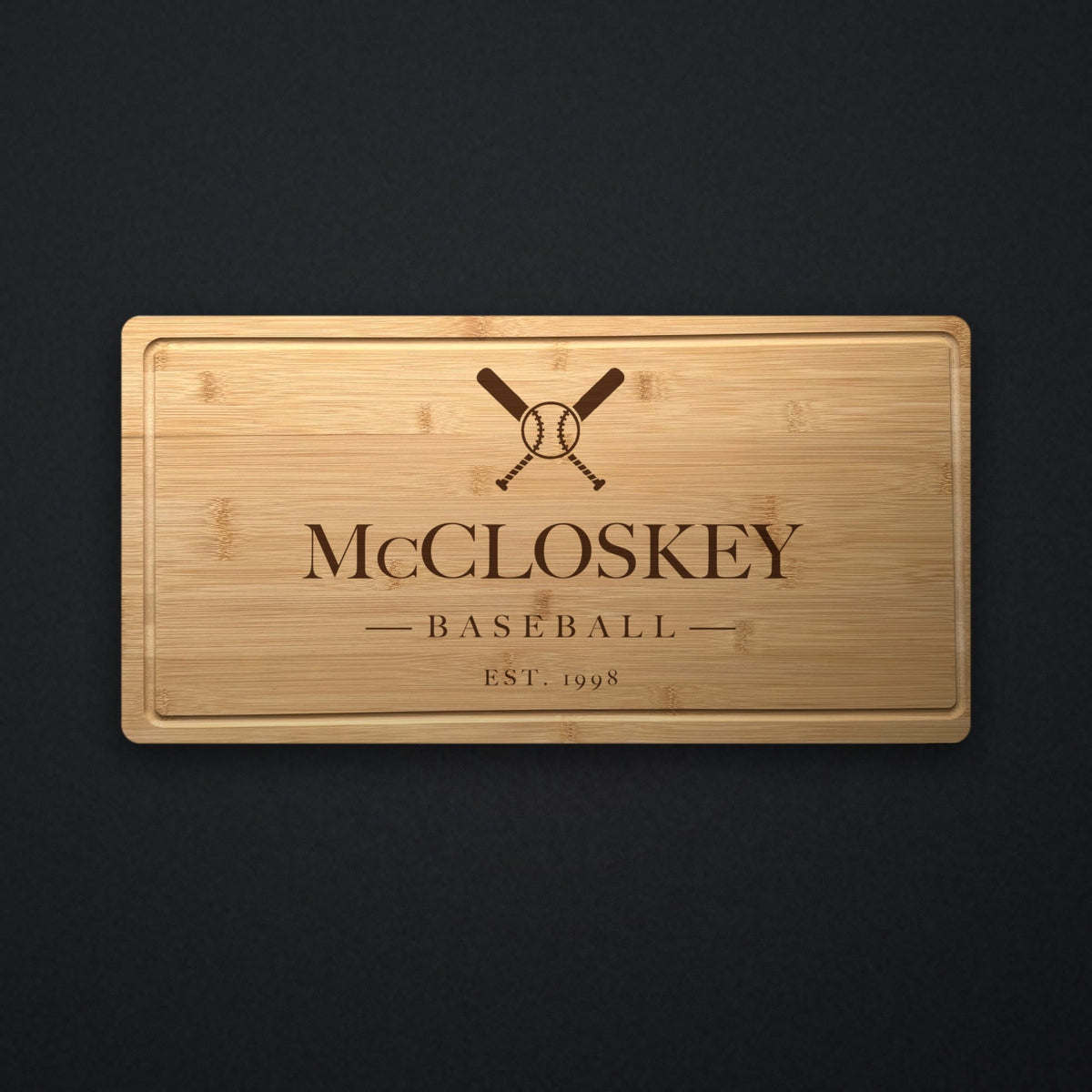 Personalized baseball coach cutting board in solid bamboo on dark slate, engraved with crossed bats and a ball above the name and the year.