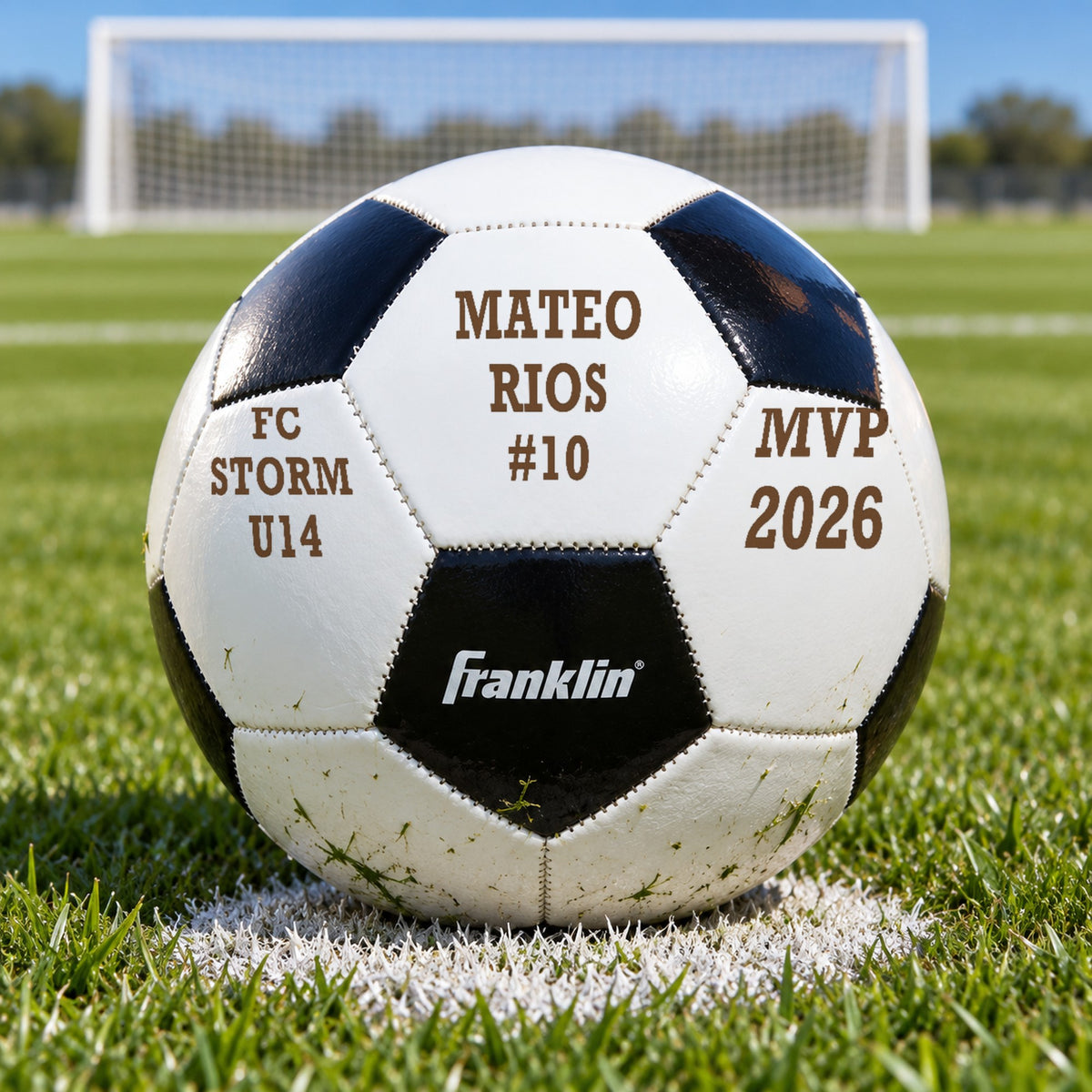 Personalized soccer ball with the name Mateo Rios and #10 engraved in the middle panel, sitting on the penalty spot of a grass soccer field