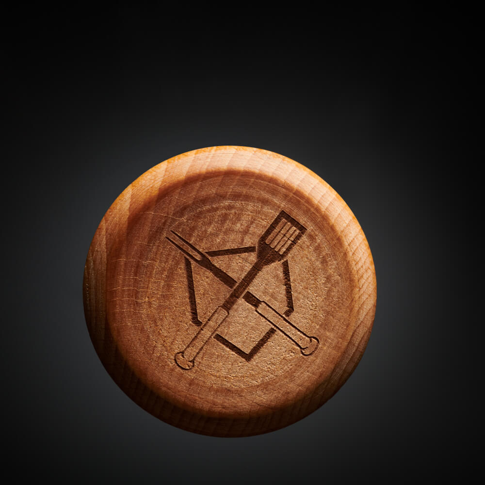 Macro of the engraved BBS bat-and-spatula crest on the bottom of the pigtail's beech wood handle on a black backdrop