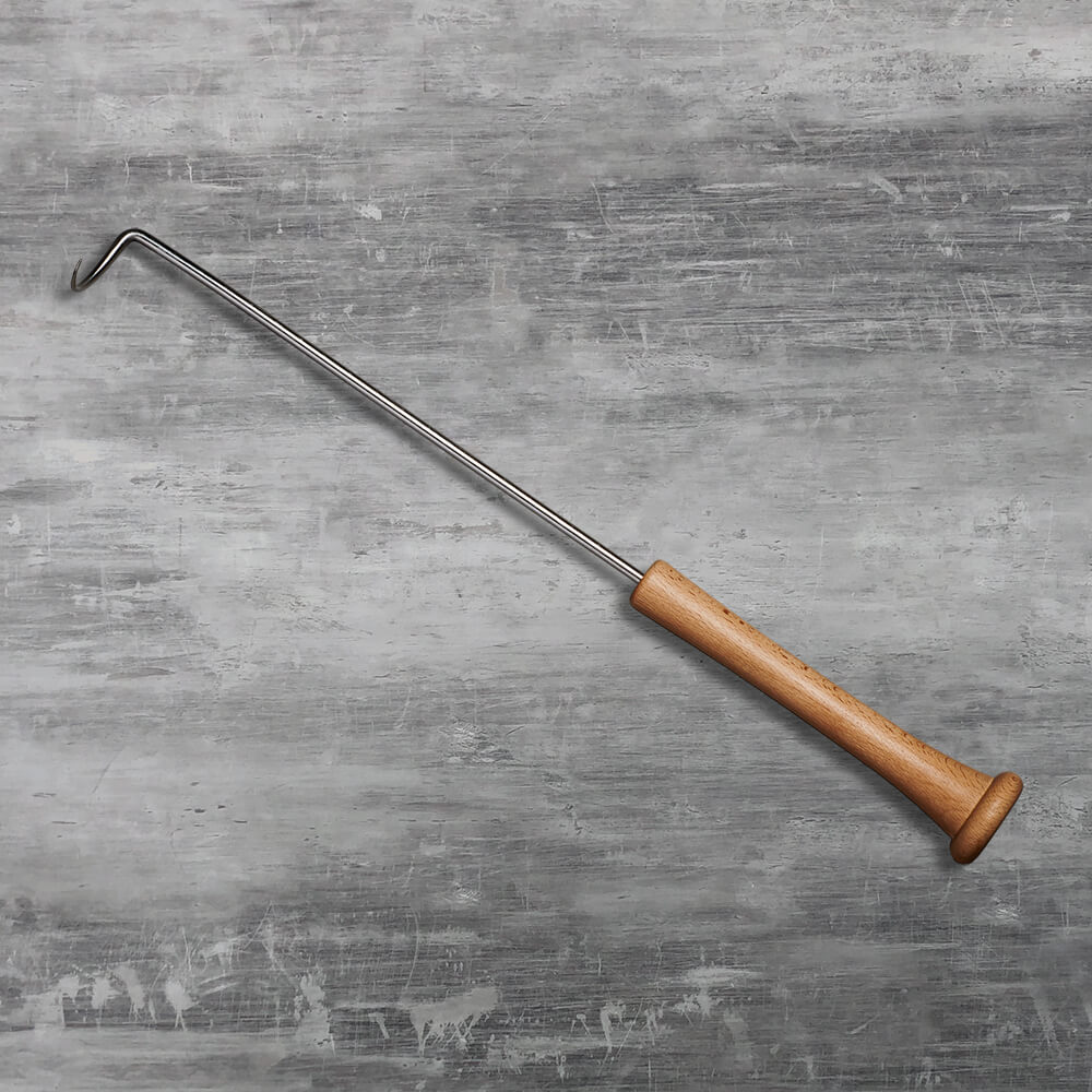 Top-down view of the pigtail meat hook laid diagonally across a grey concrete countertop showing the full bat-shaped handle