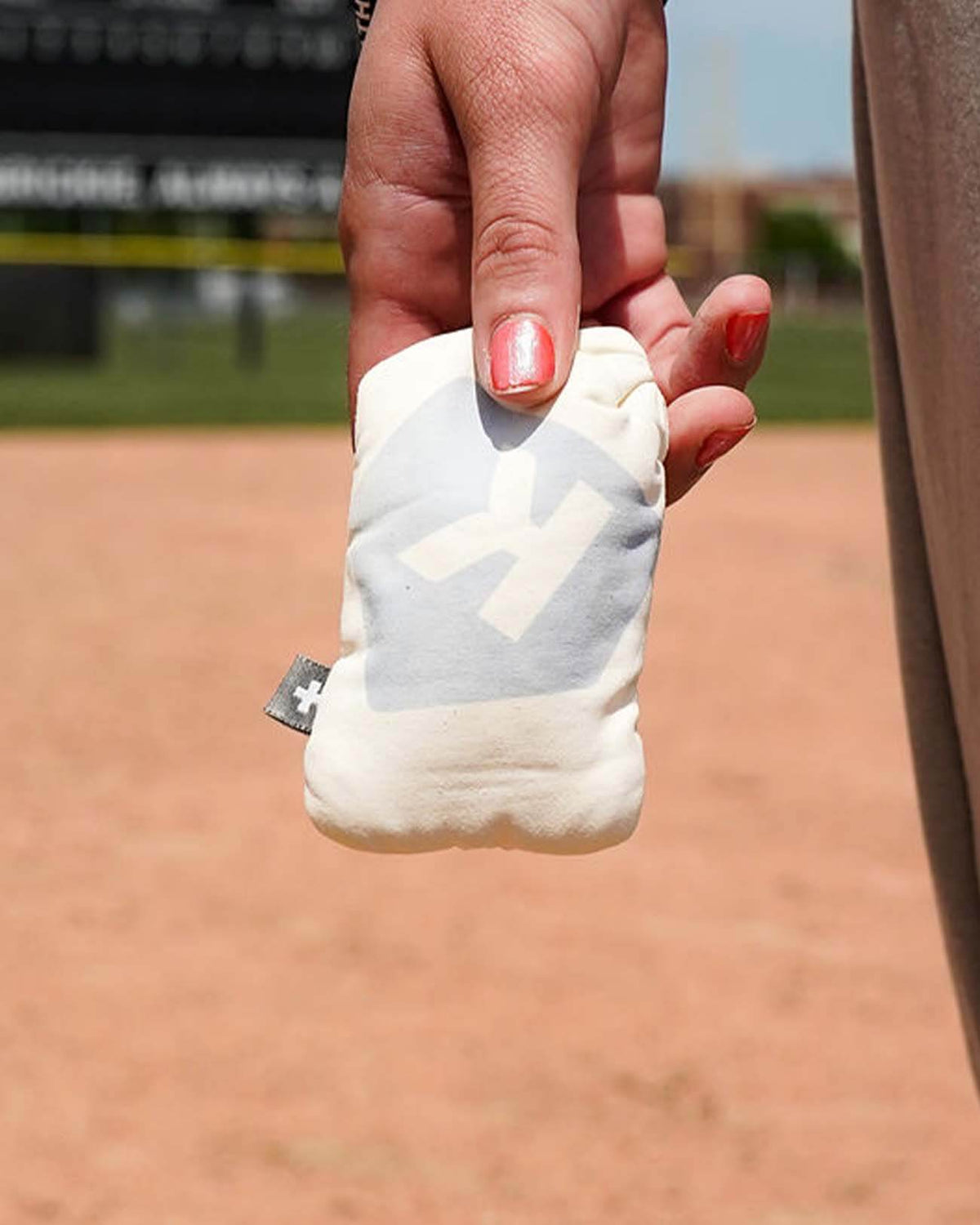 Hand holding white rosin bag with sample number printed on front, displayed on baseball field infield dirt background