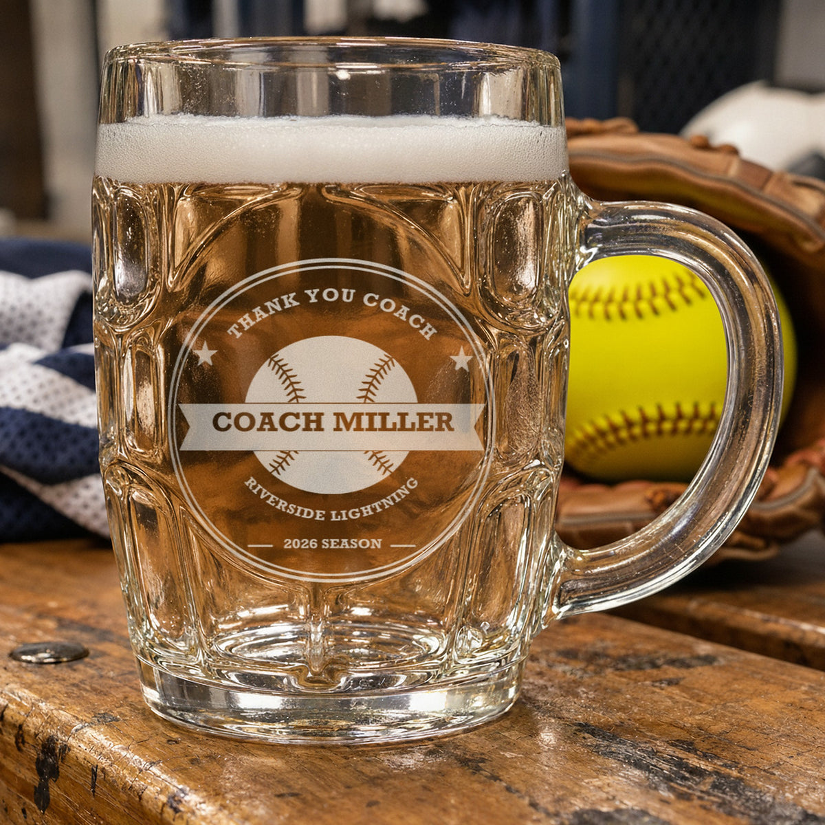 Softball coach beer stein on a dugout bench beside a yellow softball in a fastpitch glove, etched Thank You Coach, Coach Miller, Riverside Lightning, 2026 Season