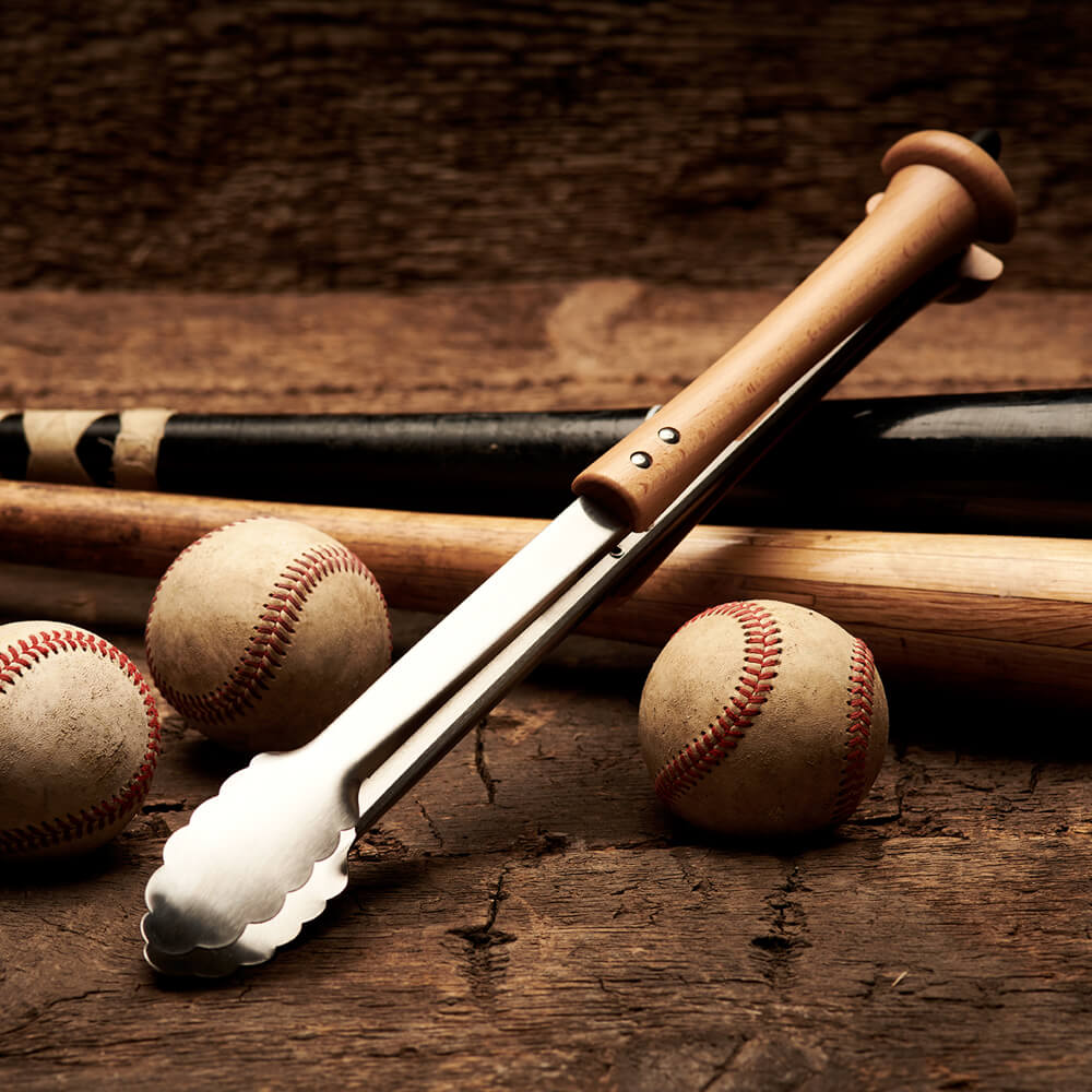 Side view of the splitfinger tongs with vintage baseballs and bats in soft focus on a rustic wood surface