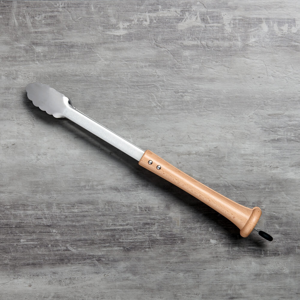 Top-down shot of the splitfinger tongs laid on a grey concrete countertop showing the full bat-grip handle and scallop-edge stainless tongs