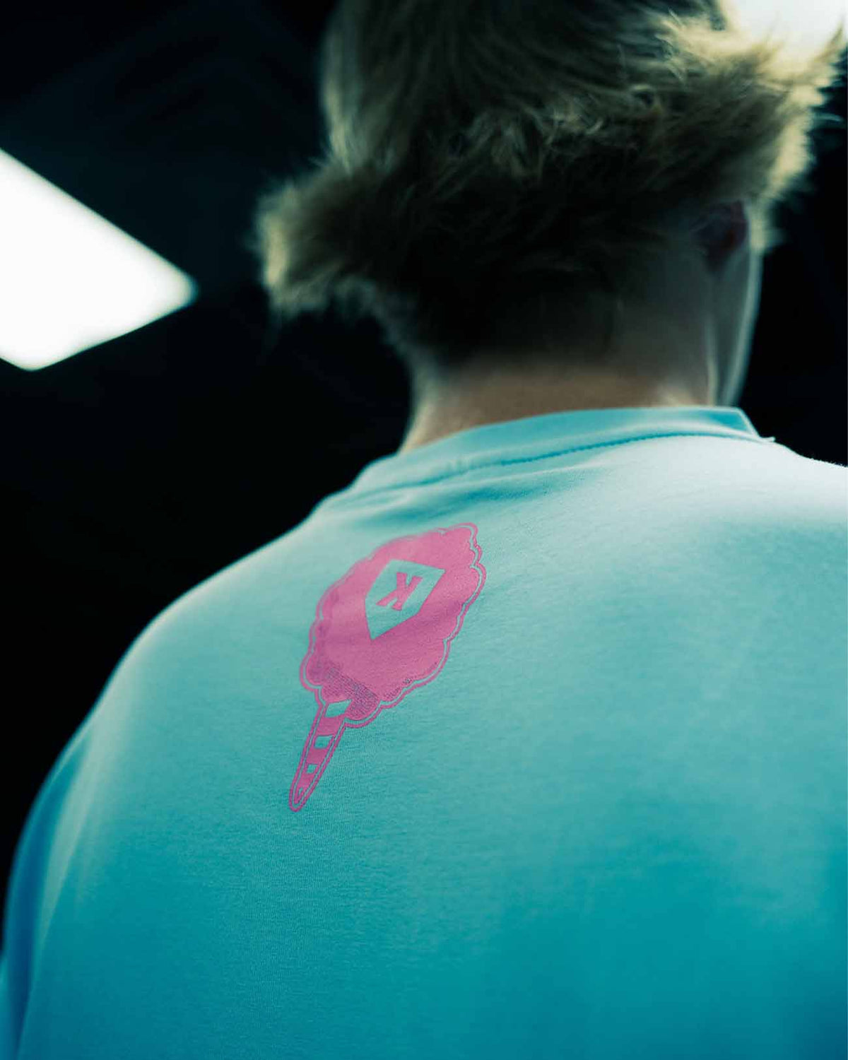 Person wearing turquoise cotton tee with pink embroidered baseball glove and pitcher logo on back shoulder area
